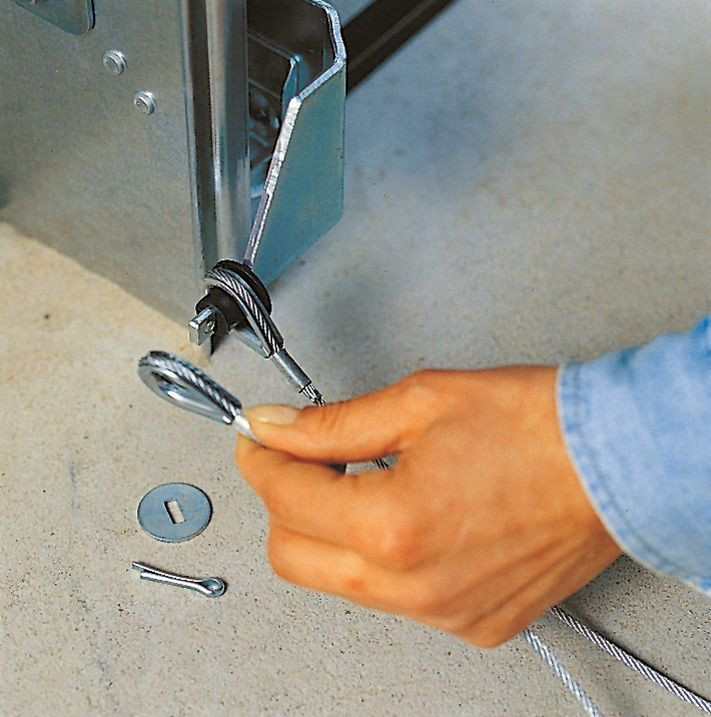 Montaż bramy segmentowej: Linkę stalową łączącą bramę ze sprężynami mocuje się na dolnym segmencie przy mocowaniu rolki