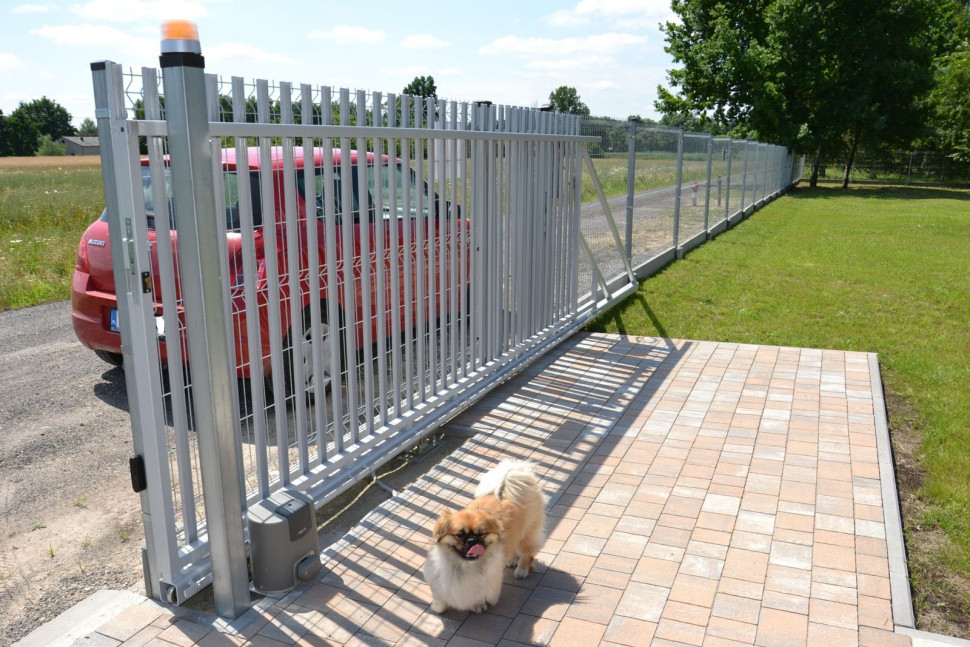 Skrzynka z motoreduktorem stoi obok słupka z lampą ostrzegawczą, na zalecanym podwyższeniu