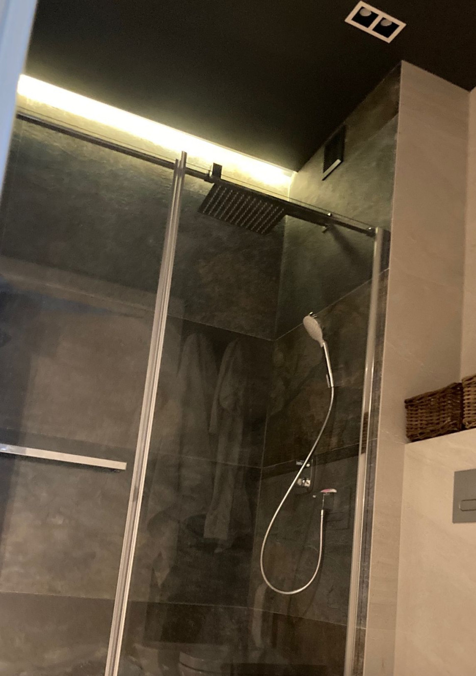 Nad wnęką z prysznicem ulokowano taśmę LED, w podwieszanym suficie (czarnym) - halogeny