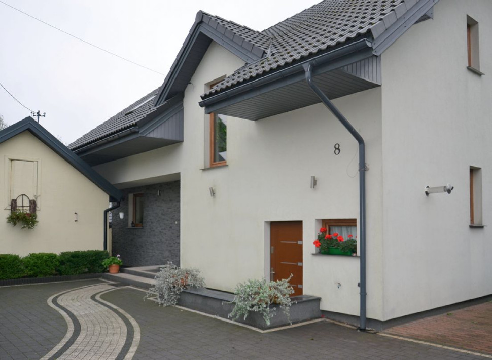 Nowy, murowany, dom (wyższy) wzniesiono obok starego. Wykończono je w podobny sposób - otynkowano zaprawą mineralną w odcieniu kremowym, pokryto dachówką cementową w kolorze grafitowym