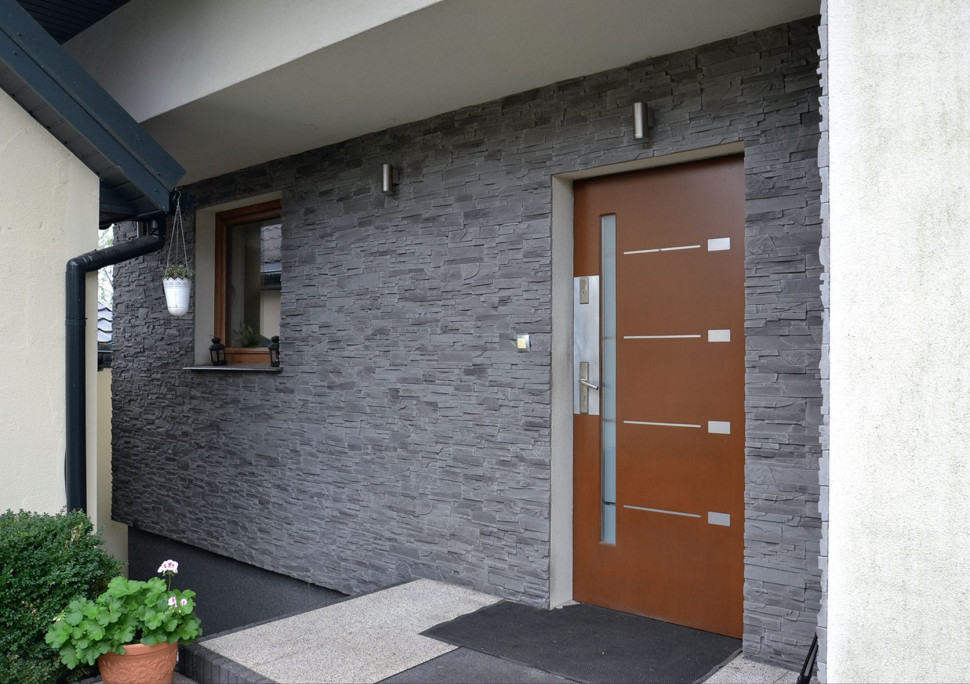 Ścianę przy głównym wejściu obłożono betonową okładziną, imitującą łupany granit