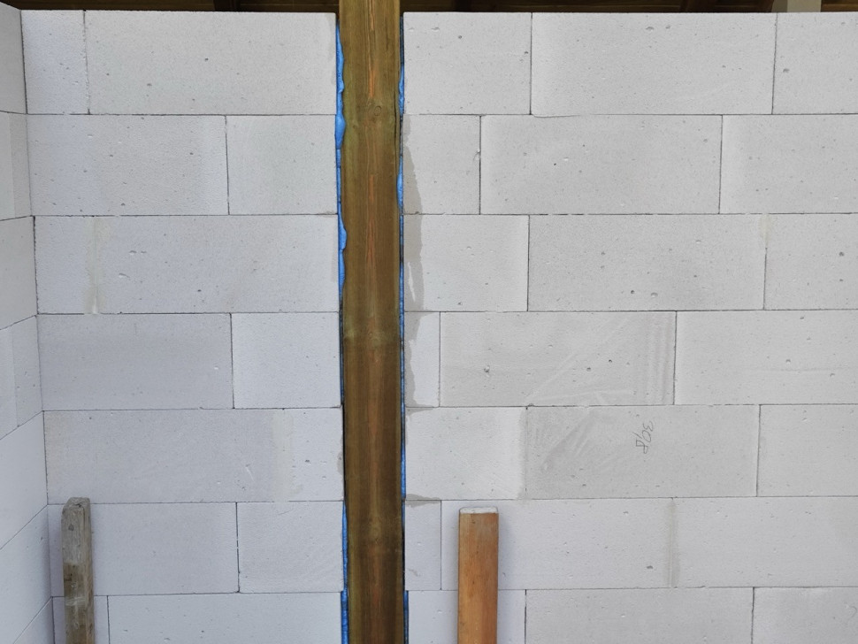 Dylatacja pionowa pomiędzy murem z betonem komórkowym a drewnianym słupem podpierającym konstrukcję dachową.